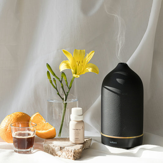a table with a vase of flowers, an orange and a bottle of essential oils